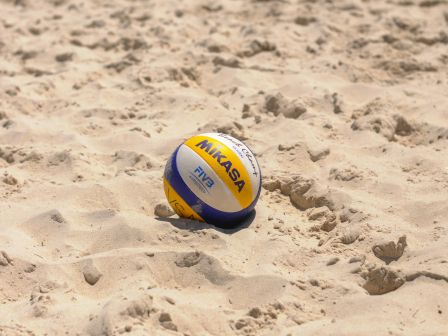 A beach volleyball is lying on sandy ground, featuring the Mikasa brand logo and FIVB (Fédération Internationale de Volleyball) markings.