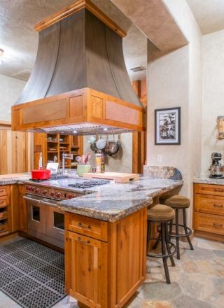 A spacious kitchen with wooden cabinets, a large island with stools, granite countertops, and a decorative range hood.