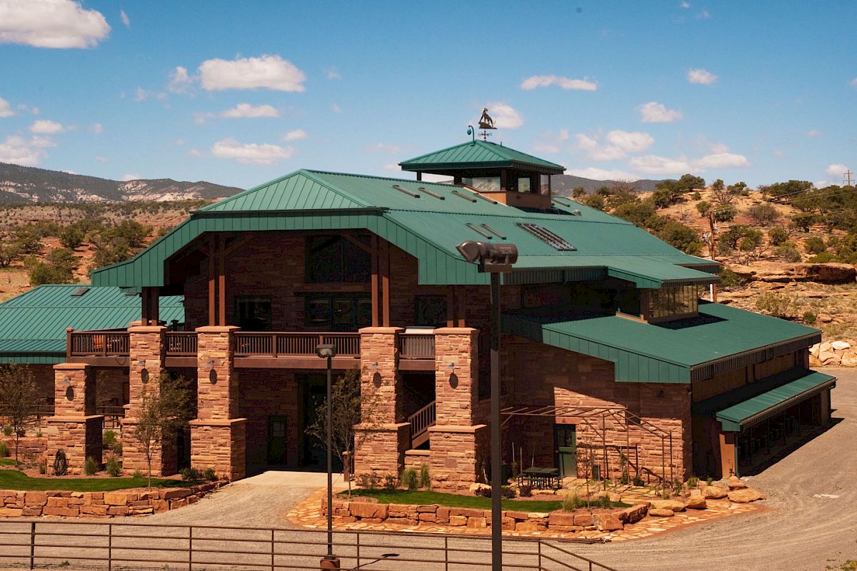 A large building with green roofs surrounded by a natural landscape under a blue sky with some clouds.