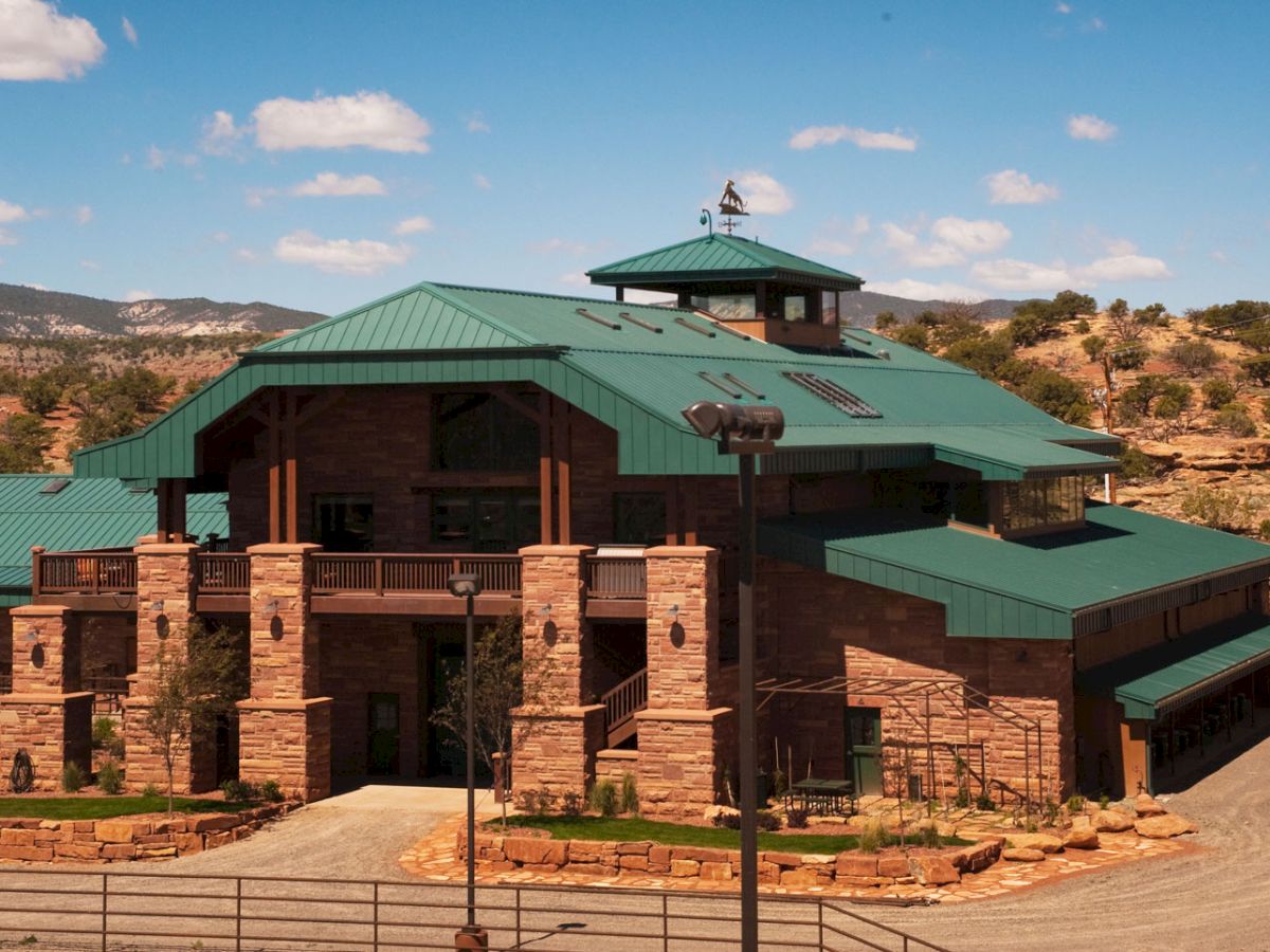 A large building with green roofs surrounded by a natural landscape under a blue sky with some clouds.