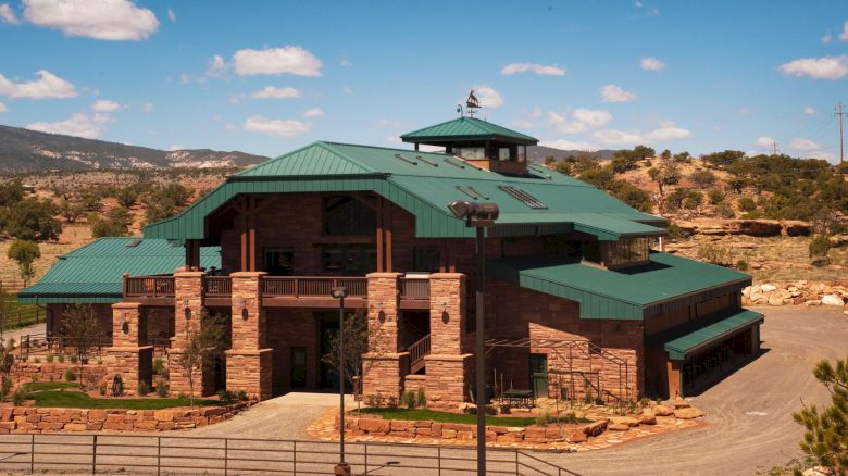 A large building with green roofs surrounded by a natural landscape under a blue sky with some clouds.