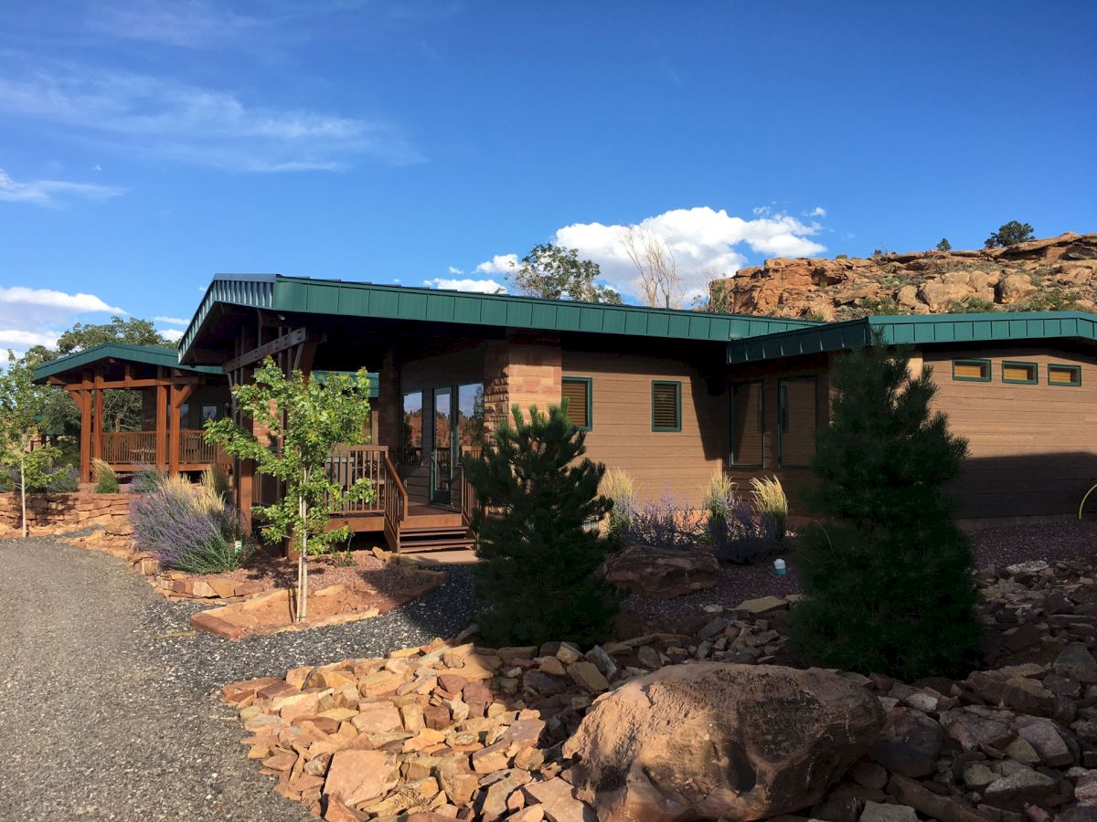 A modern, single-story building with a green roof, surrounded by rocks and trees under a clear blue sky.