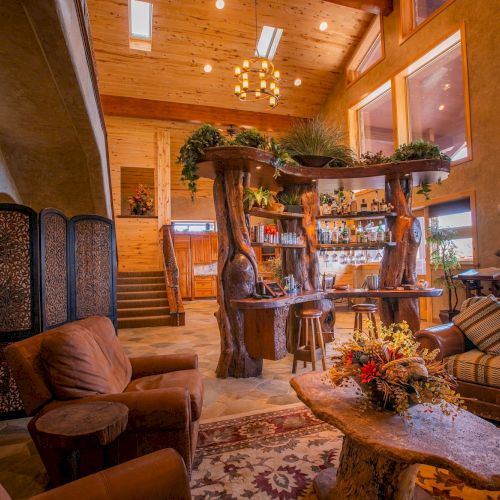 A cozy, rustic living room with warm wood walls, carved wooden furniture, a floral centerpiece, and comfortable seating under soft lighting.