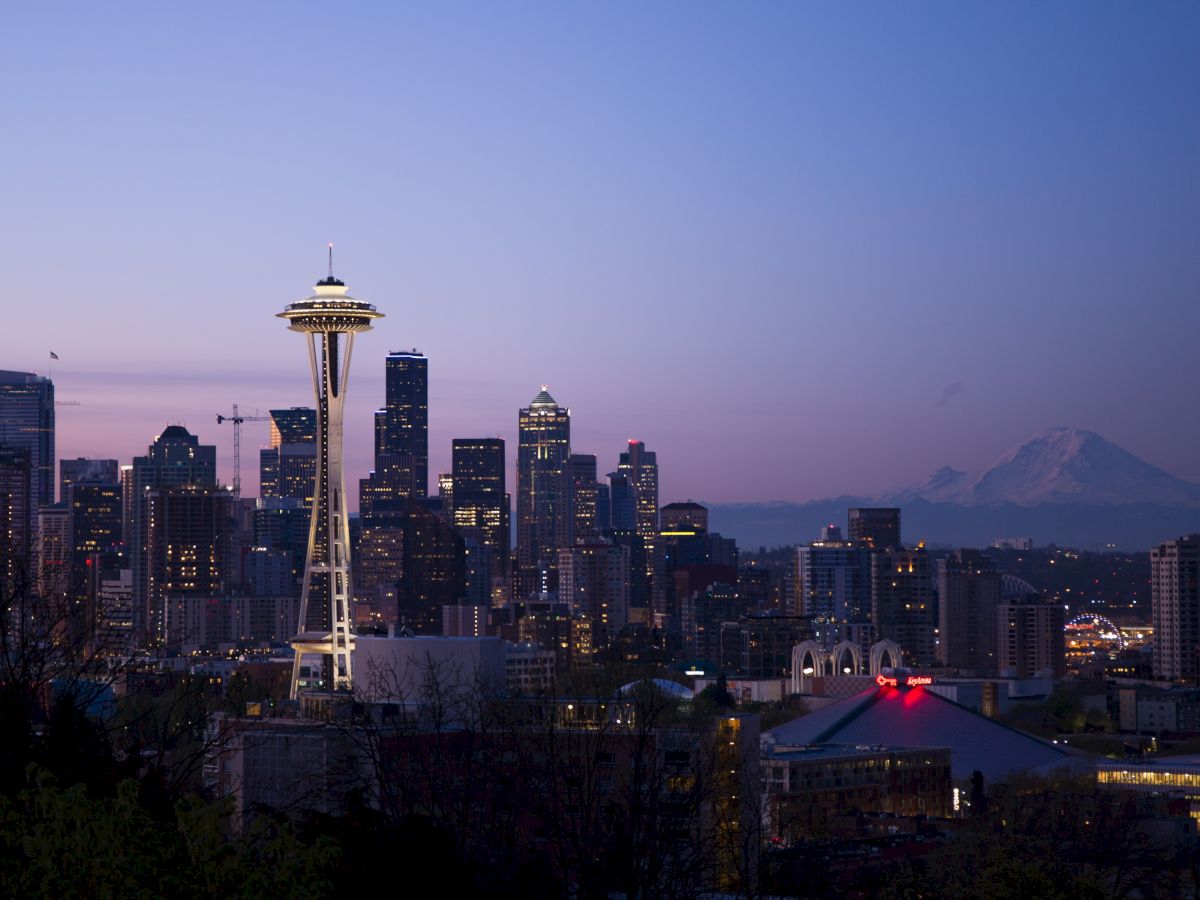 Seattle skyline at dusk with the Space Needle lit up and Mount Rainier visible in the background against a fading twilight sky.